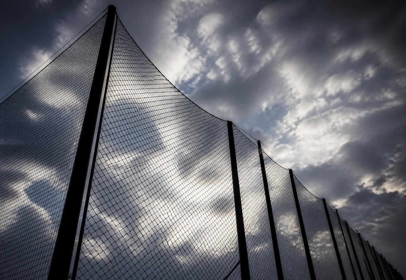 Tall black ball stop netting on steel poles against a dramatic sky